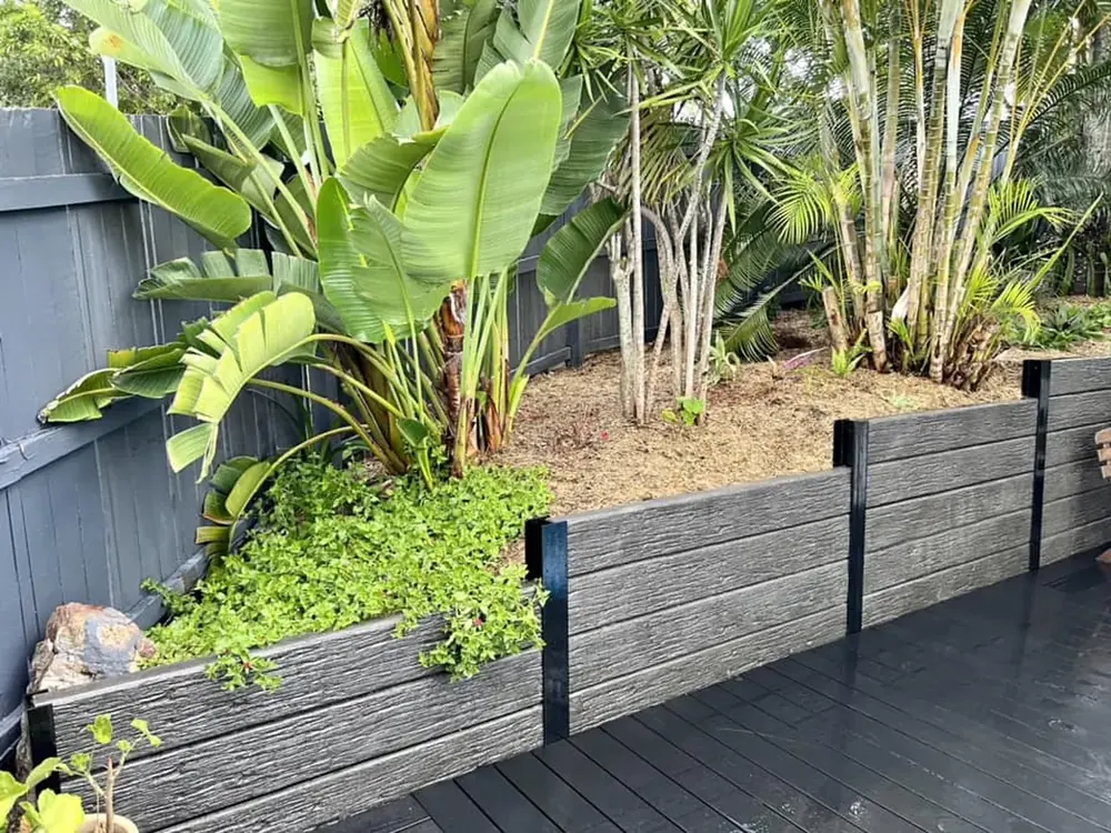 Charcoal concrete sleeper retaining wall with steel posts holding a raised garden bed